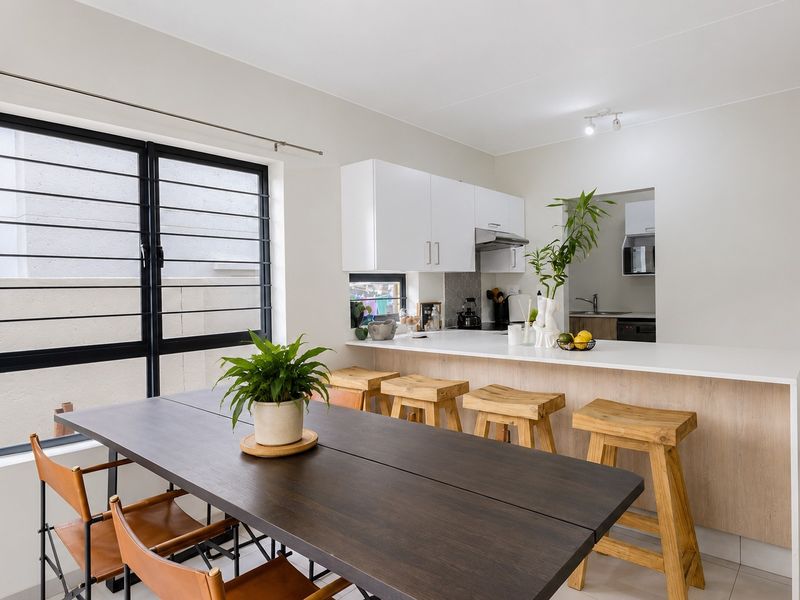 Modern open-plan kitchen and dining area featuring a breakfast bar, sleek white cabinetry, and large windows with security bars.