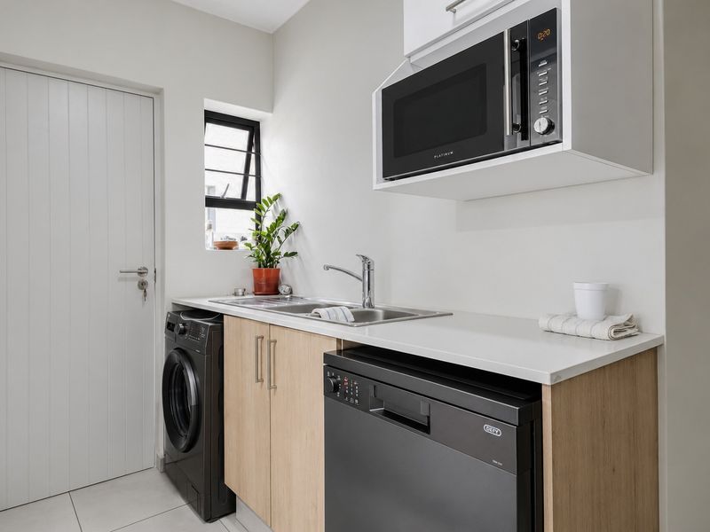 A functional scullery featuring modern cabinetry, a stainless steel sink, built-in microwave, and dedicated space for laundry and dishwashing appliances.