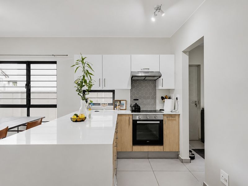 Modern kitchen featuring sleek white cabinetry, quartz countertops, a hexagonal tile backsplash, and integrated stainless steel appliances, flowing into an open-plan living area.
