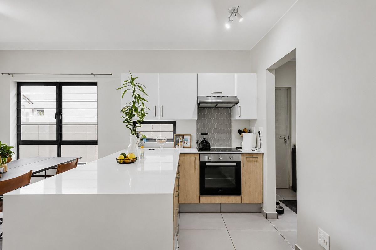 Modern kitchen featuring sleek white cabinetry, quartz countertops, a hexagonal tile backsplash, and integrated stainless steel appliances, flowing into an open-plan living area.