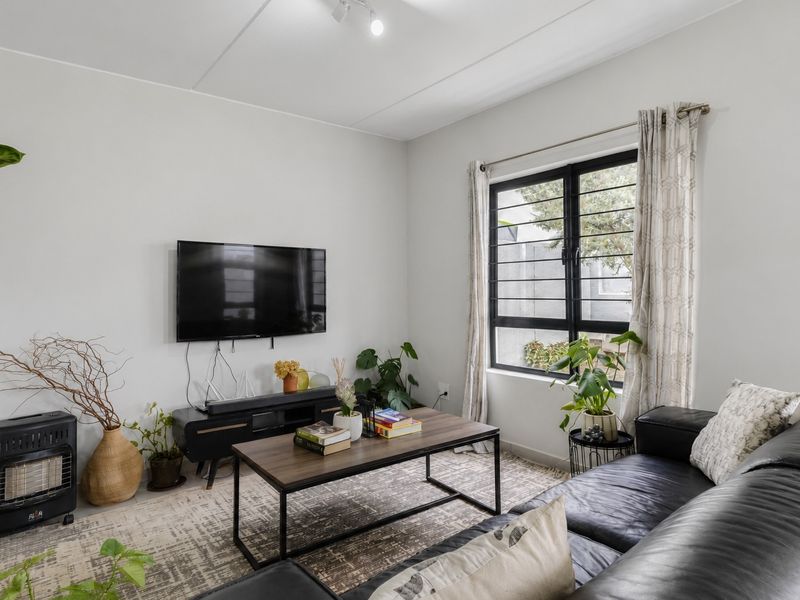 A well-lit living room featuring a large window with security bars, neutral walls, and a functional layout suitable for comfortable seating.
