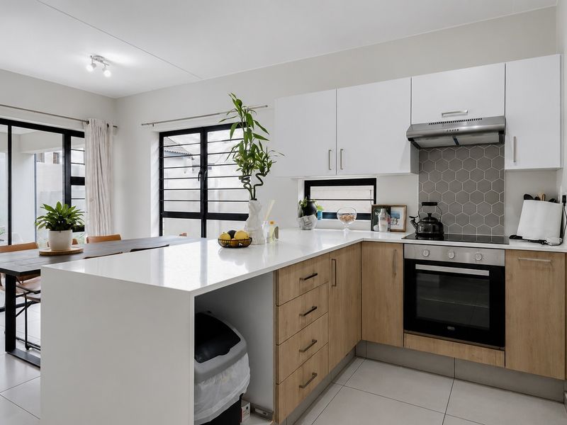 Modern open-plan kitchen and dining area featuring sleek cabinetry, stone countertops, integrated appliances, and large sliding doors leading to the outdoor space.