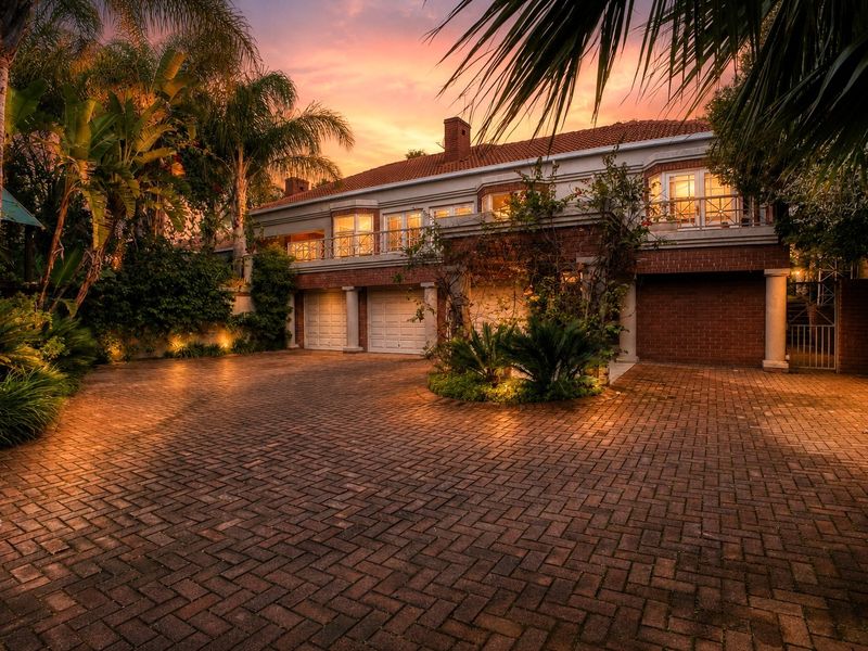 A well-maintained multi-car garage facade featuring brick paving, a balcony, and classic architectural detailing, captured at sunset.