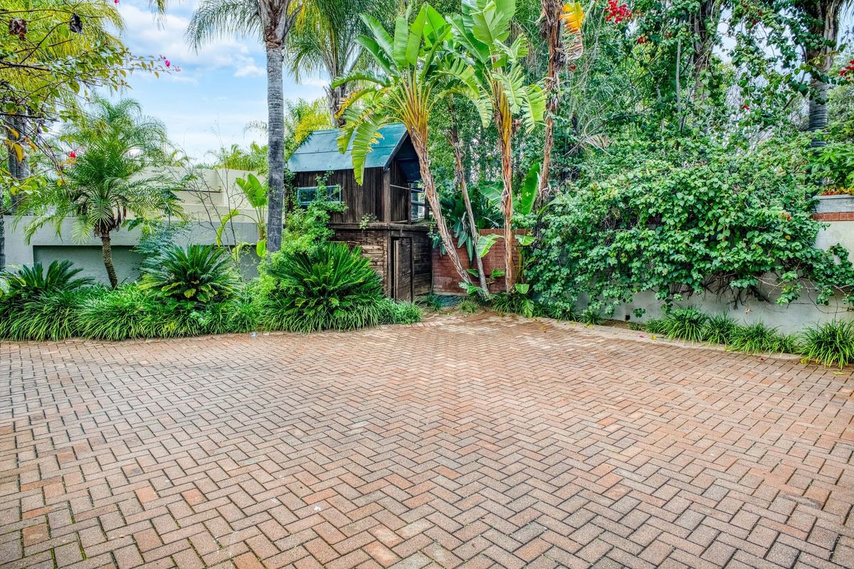 A paved rear courtyard area featuring established garden landscaping, mature trees, and a boundary wall.