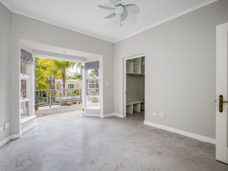 Bright bedroom featuring polished concrete floors, a ceiling fan, a walk-in closet, and direct access to a private balcony through a bay window.
