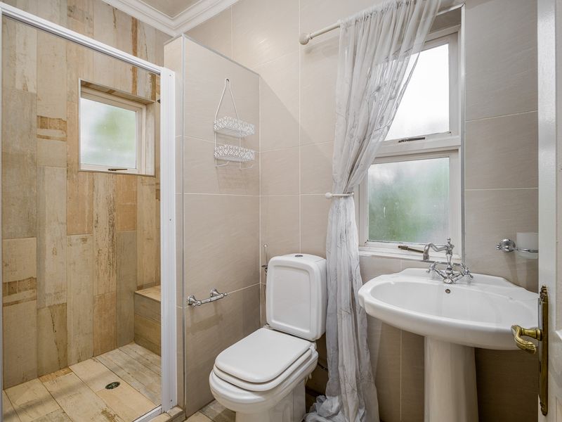 A functional bathroom featuring a walk-in shower, pedestal basin, and toilet with neutral wall and floor tiling.