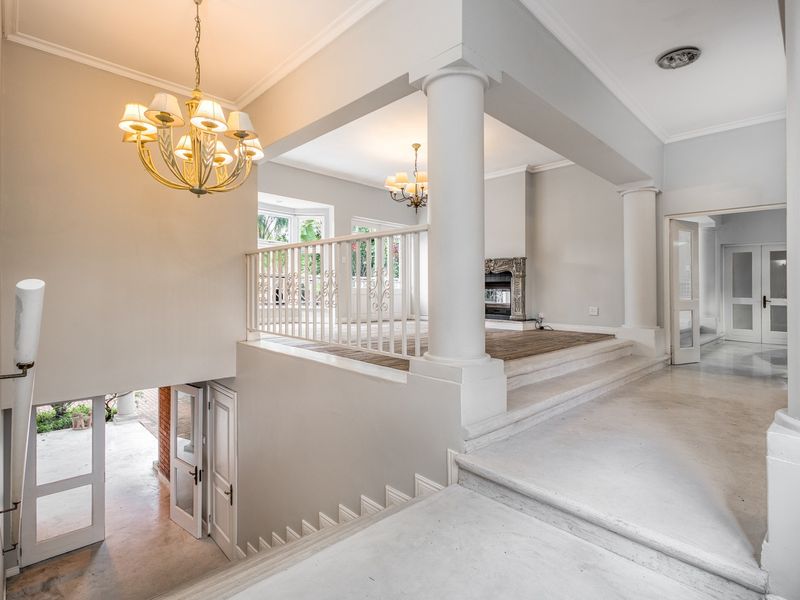 Spacious split-level living area featuring elegant columns, a fireplace, classic chandeliers, and a grand staircase leading to the lower level.