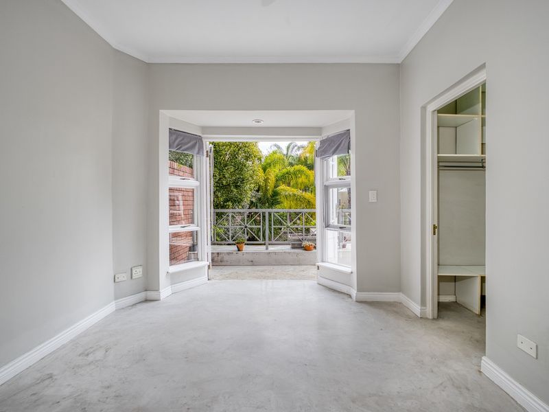 A bright, empty bedroom featuring polished concrete floors, a built-in closet, and a bay window opening onto a private balcony.