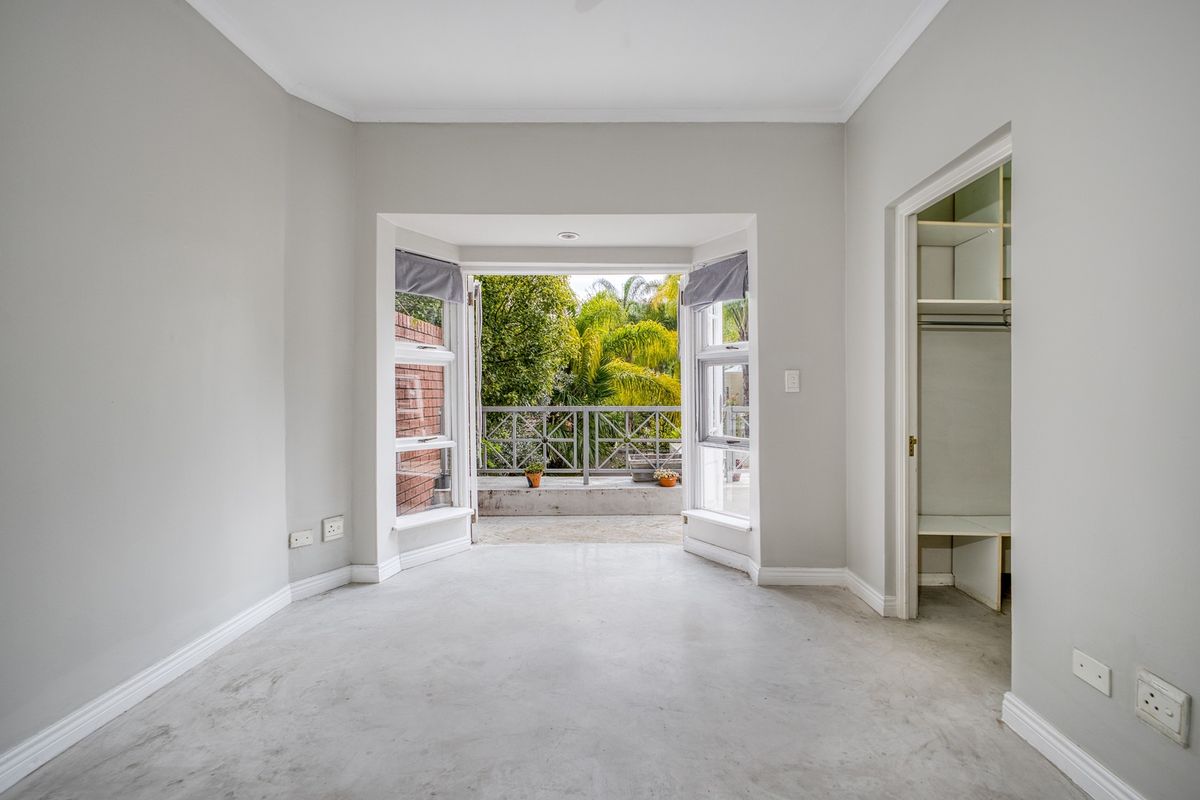 A bright, empty bedroom featuring polished concrete floors, a built-in closet, and a bay window opening onto a private balcony.