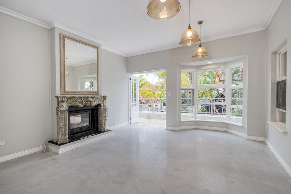 Spacious living room featuring polished concrete floors, an ornate fireplace, bay windows, and direct access to an outdoor balcony area.