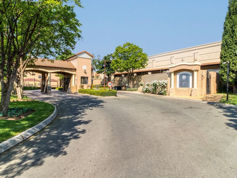 The secure entrance to the apartment complex features a well-maintained gatehouse, landscaped gardens, and paved driveway access.