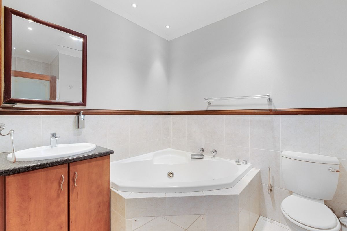 A clean bathroom featuring a corner bathtub, vanity with basin, and toilet, finished with neutral wall tiles and recessed lighting.