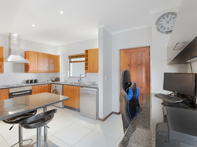 Open plan kitchen featuring wooden cabinetry, granite countertops, and integrated appliances, seamlessly flowing into a dedicated built-in workspace area.