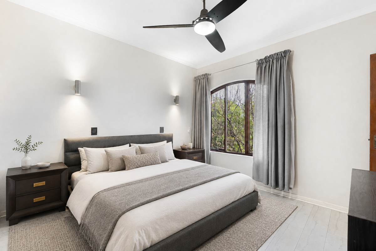 A well-maintained bedroom featuring a ceiling fan, modern wall sconces, and an arched window with neutral finishes.