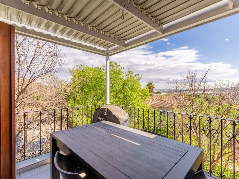 A covered balcony featuring a corrugated metal roof and decorative wrought iron railings, offering an elevated view of the surrounding neighborhood and trees.
