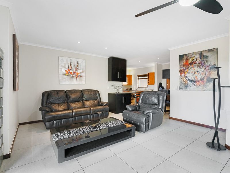 Open-plan living area featuring neutral tiled flooring, recessed lighting, a ceiling fan, and a functional kitchen with built-in cabinetry and a breakfast bar.