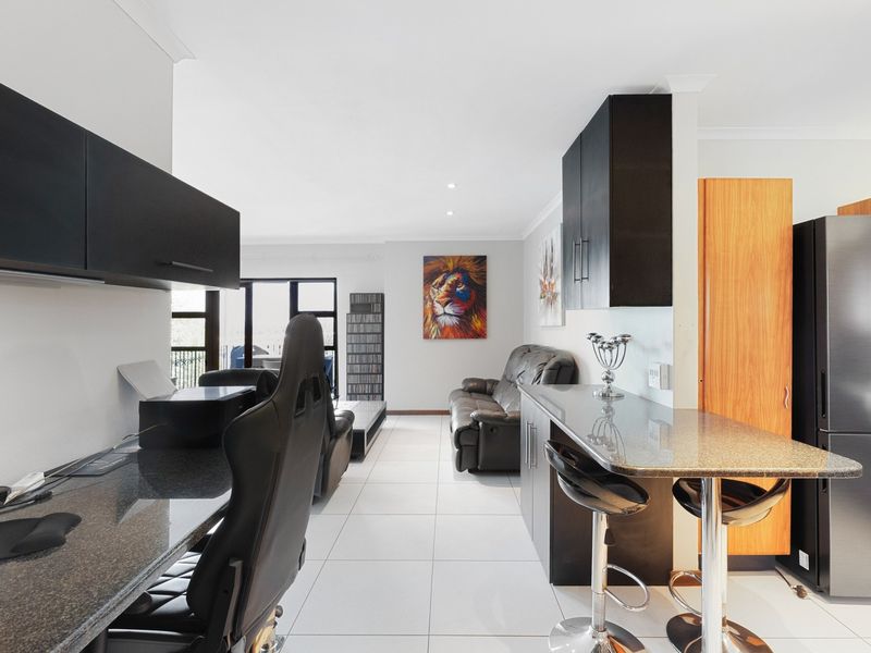 An open-plan living and kitchen area featuring modern dark cabinetry, granite countertops, a breakfast bar, and neutral tiled flooring throughout.