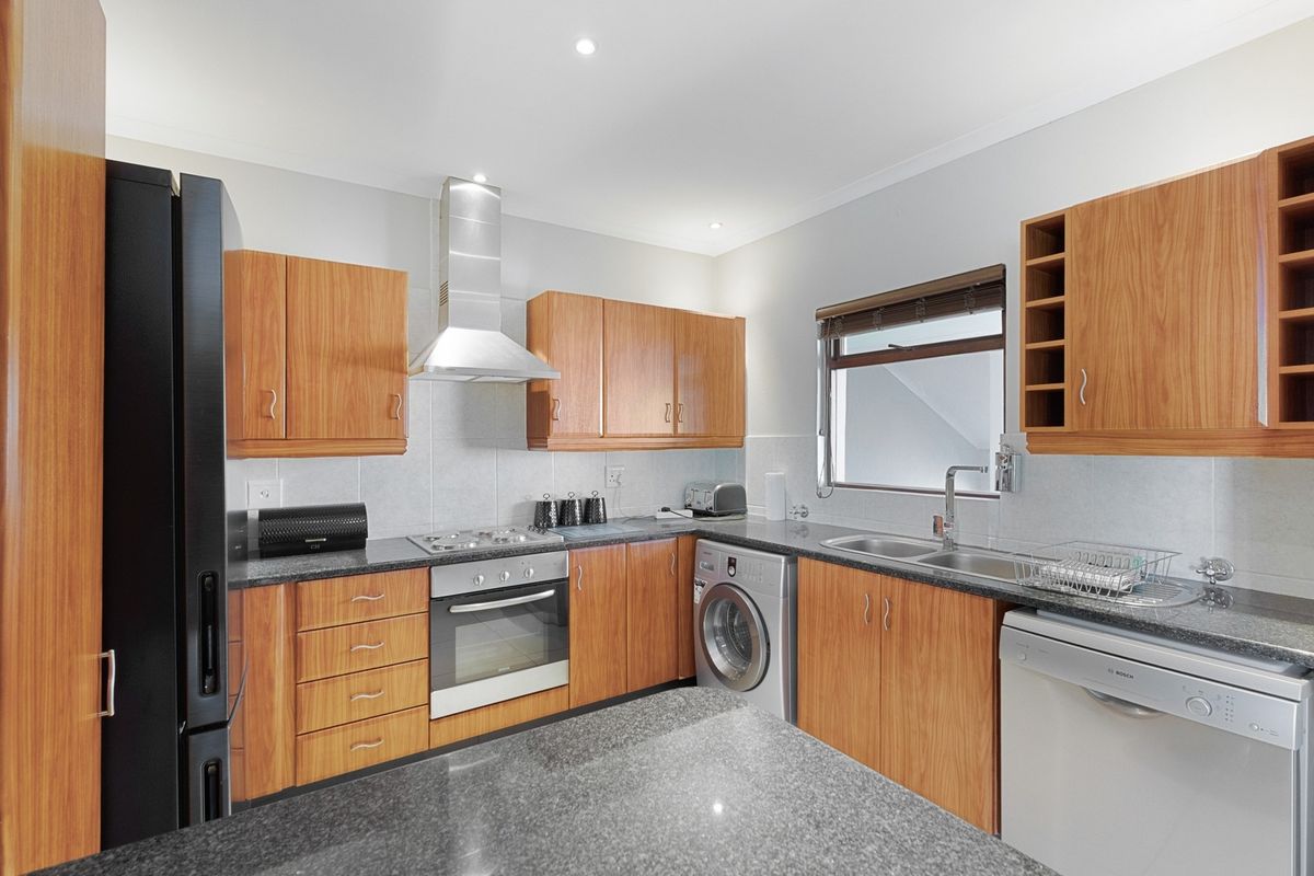 A functional kitchen featuring wooden cabinetry, granite countertops, stainless steel appliances, and a double sink with a window for natural light.