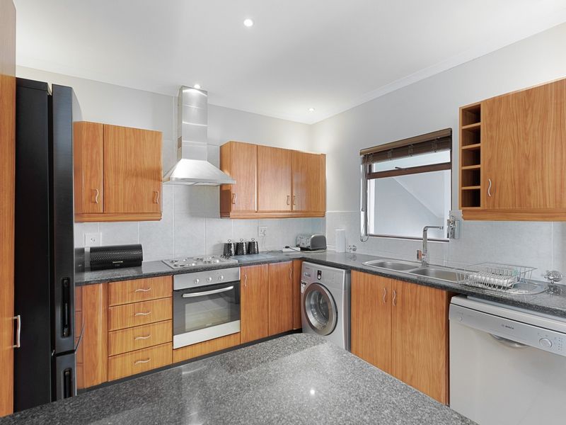 A functional kitchen featuring wooden cabinetry, granite countertops, stainless steel appliances, and a double sink with a window for natural light.