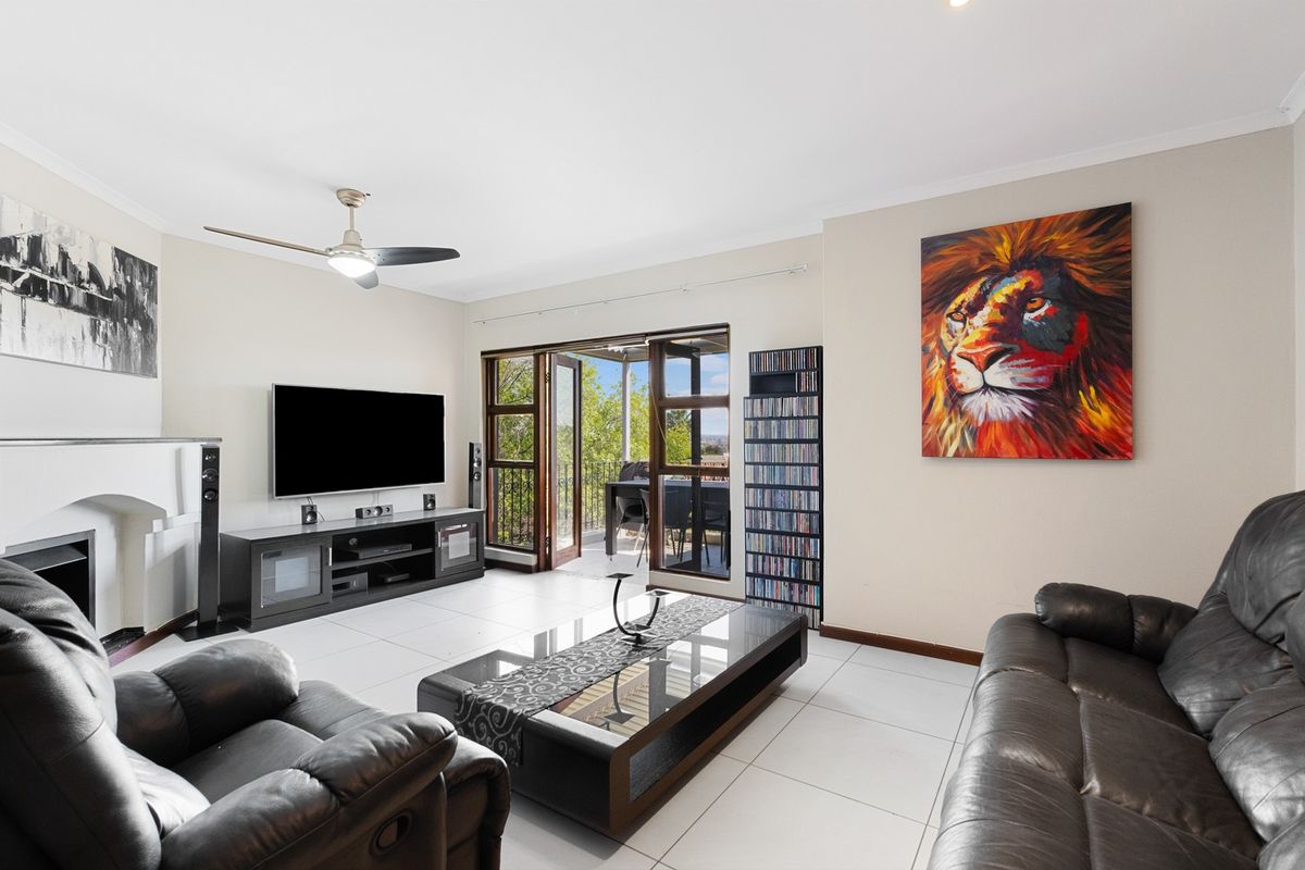 Spacious living room featuring neutral tiled flooring, a ceiling fan, and direct access to an outdoor balcony through double doors.
