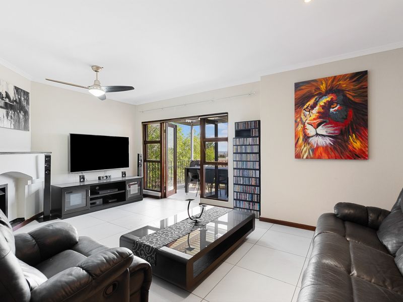 Spacious living room featuring neutral tiled flooring, a ceiling fan, and direct access to an outdoor balcony through double doors.