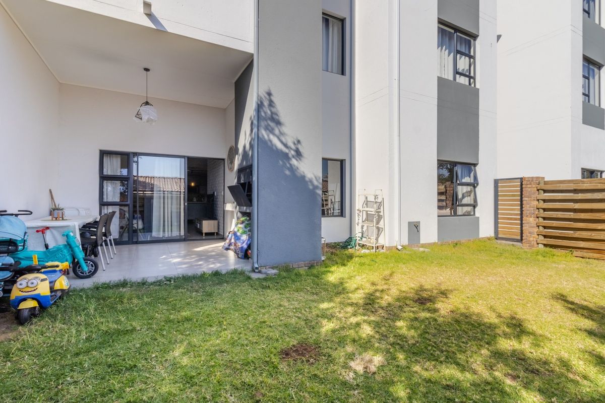 Rear view of the apartment featuring a covered patio with a built-in braai, tiled flooring, and a private garden area with timber fencing.