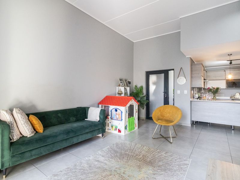 An open-plan living area featuring modern tiled floors, neutral grey walls, and a functional kitchen with built-in cabinetry and integrated appliances.