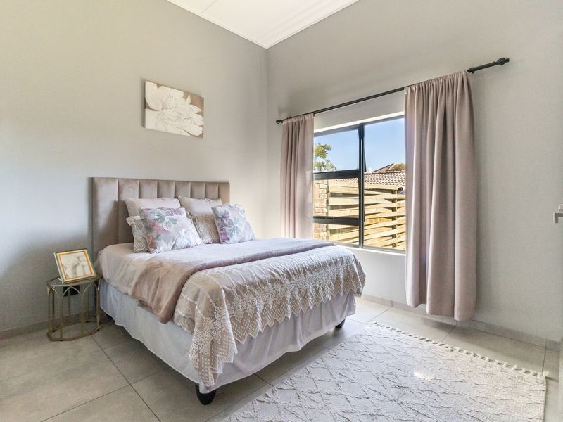 A well-maintained bedroom featuring neutral tiled flooring and a large window with natural light.