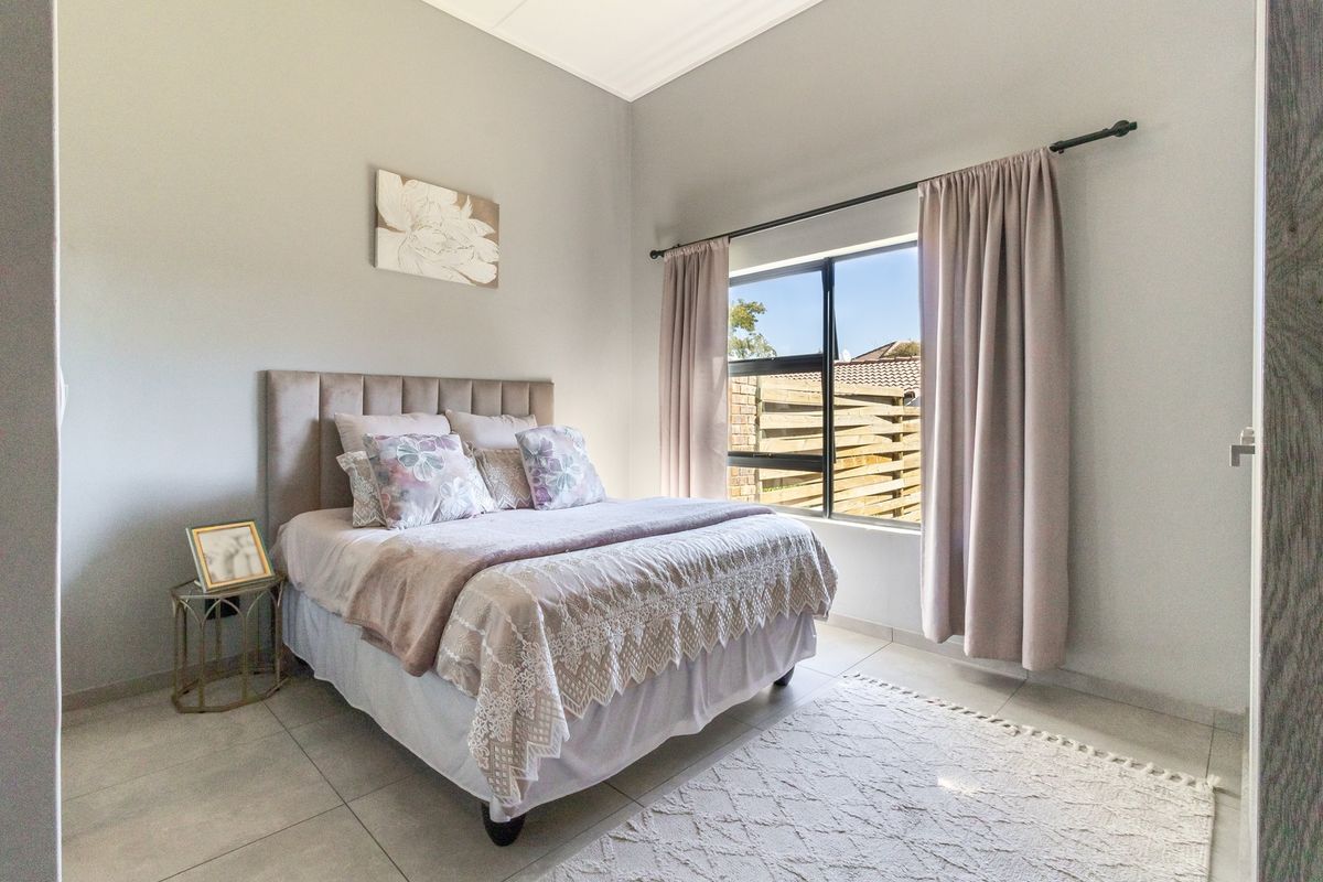 A well-maintained bedroom featuring neutral tiled flooring and a large window with natural light.