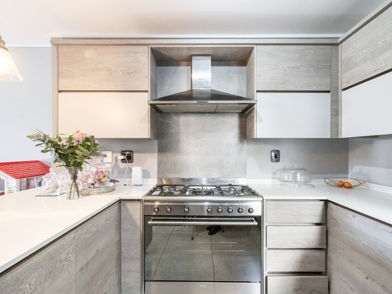 Modern kitchen featuring light wood-grain cabinetry, stone countertops, a gas stove with stainless steel extractor fan, and contemporary pendant lighting.