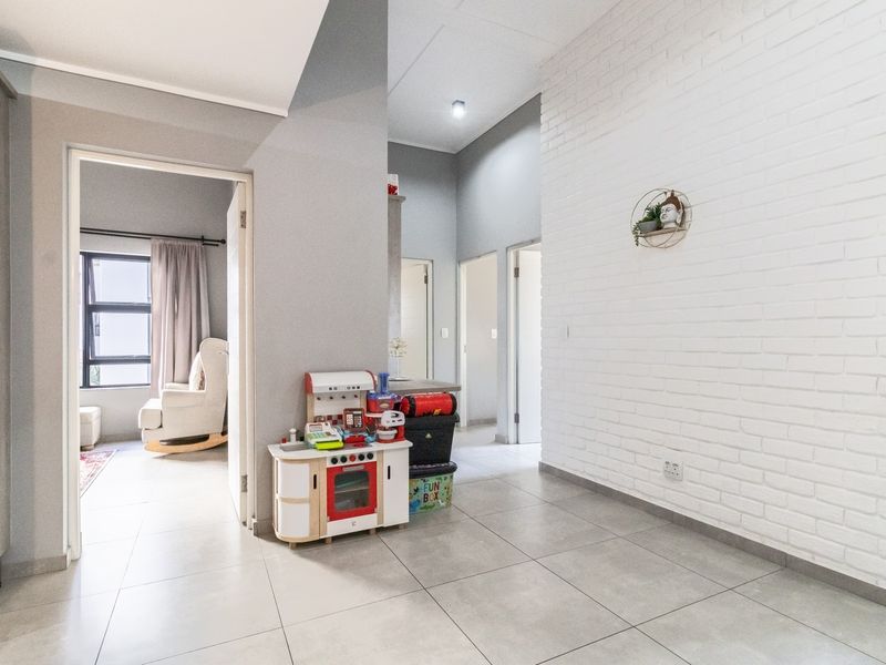 A bright, modern hallway featuring large format floor tiles, a white painted exposed brick feature wall, and access to multiple rooms.