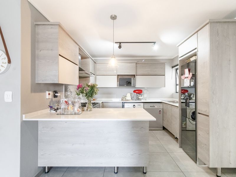Modern kitchen featuring light wood-grain cabinetry, stone countertops, integrated appliances, and a functional breakfast bar layout with contemporary lighting.