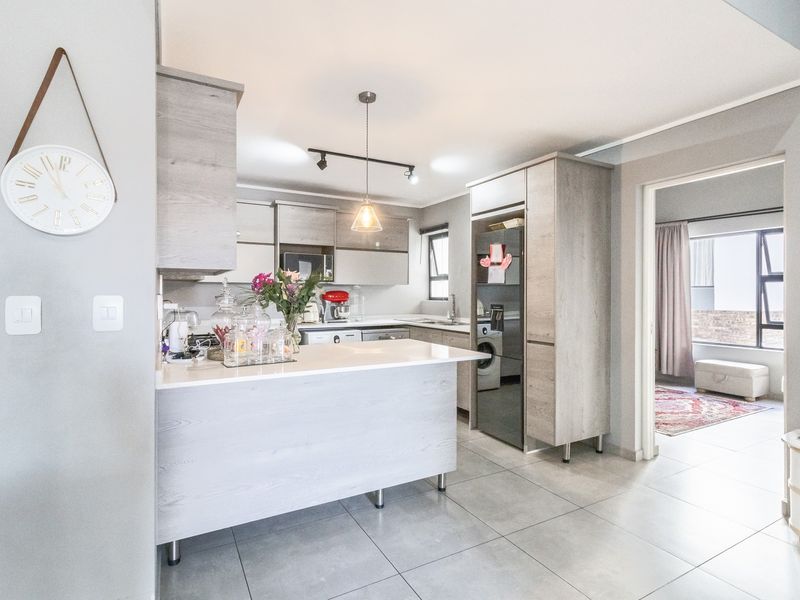 Modern kitchen featuring light wood-grain cabinetry, stone countertops, a breakfast bar, and integrated appliances, with tiled flooring and contemporary lighting.