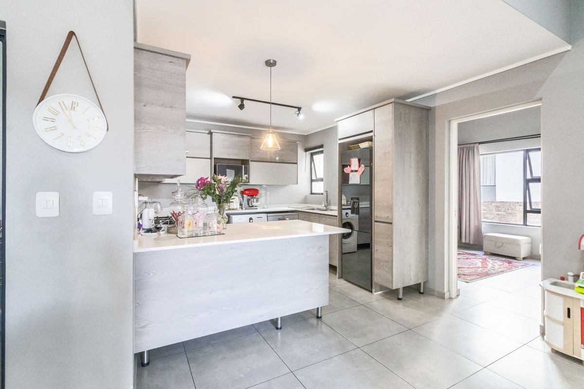 Modern kitchen featuring light wood-grain cabinetry, stone countertops, a breakfast bar, and integrated appliances, with tiled flooring and contemporary lighting.