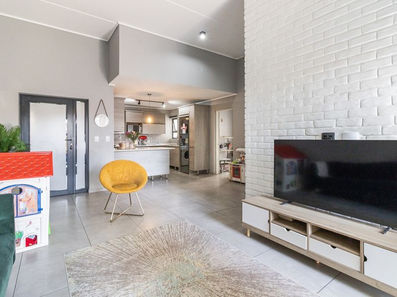 Spacious open-plan living area featuring a white exposed brick feature wall, neutral tiled flooring, and a modern kitchen with integrated cabinetry.