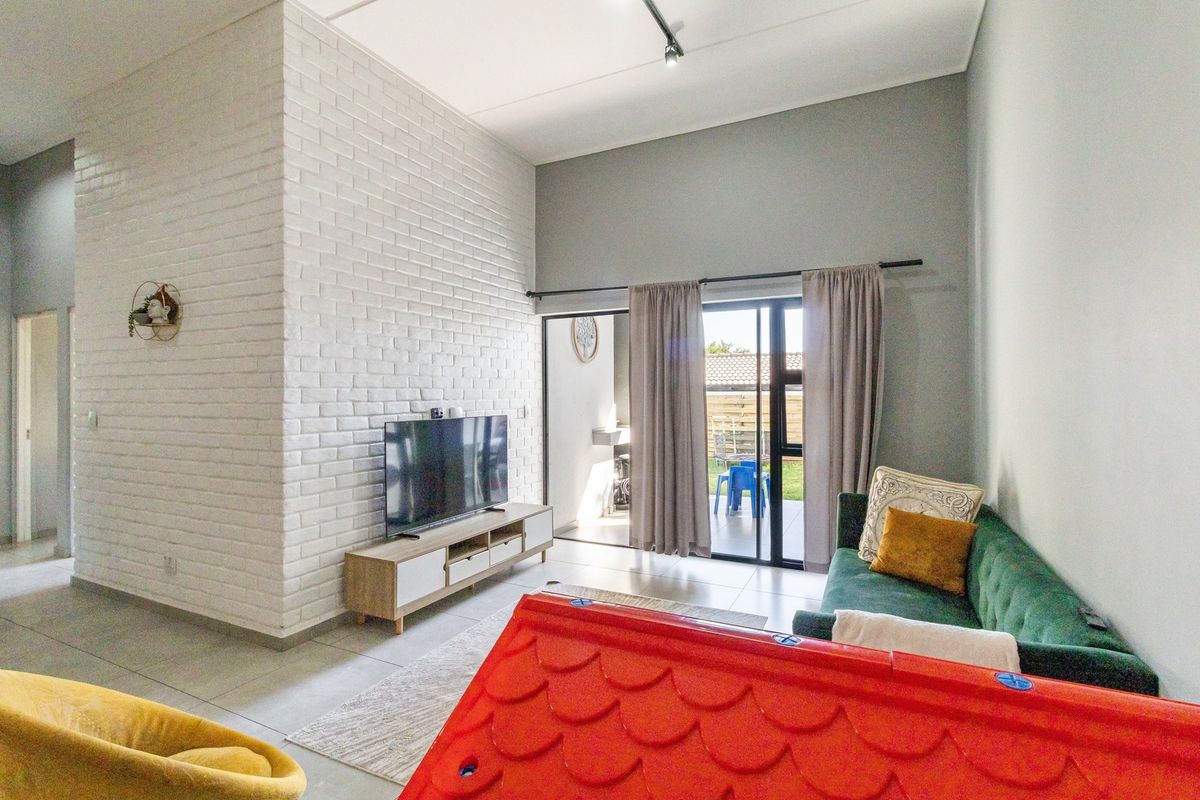 Modern living room featuring a white exposed brick accent wall, high ceilings, and large sliding glass doors providing access to the outdoor patio area.