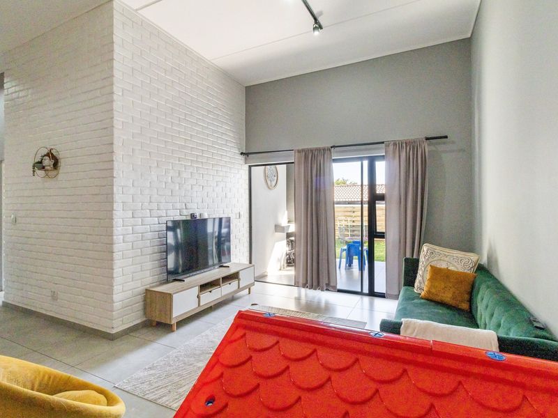 Modern living room featuring a white exposed brick accent wall, high ceilings, and large sliding glass doors providing access to the outdoor patio area.