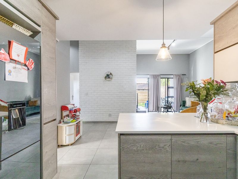 Modern open-plan living area featuring a kitchen island, sleek cabinetry, tiled floors, and an exposed brick feature wall leading to an outdoor patio.