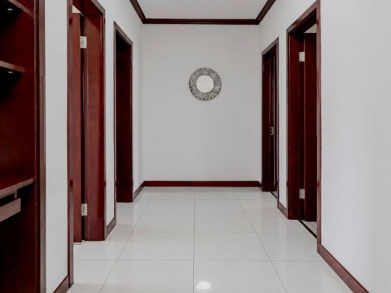 A clean, well-maintained hallway featuring dark wood trim, crown molding, tiled flooring, and built-in shelving.