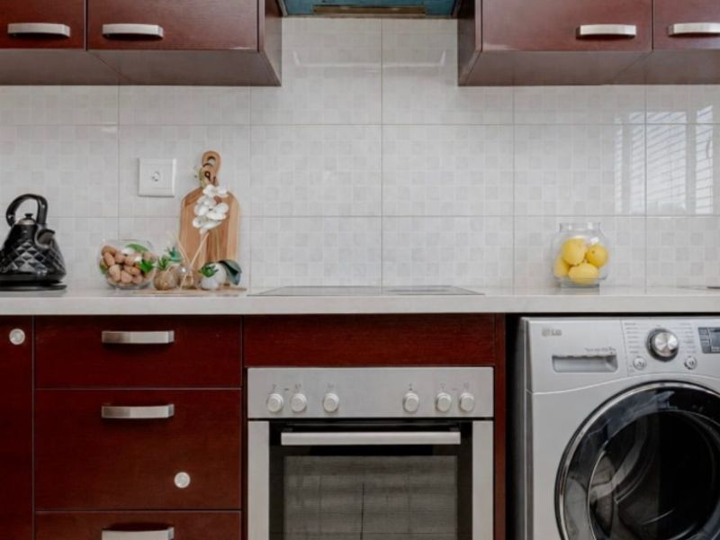 A functional kitchen featuring dark wood cabinetry, stone countertops, a built-in oven with hob, and an integrated washing machine.