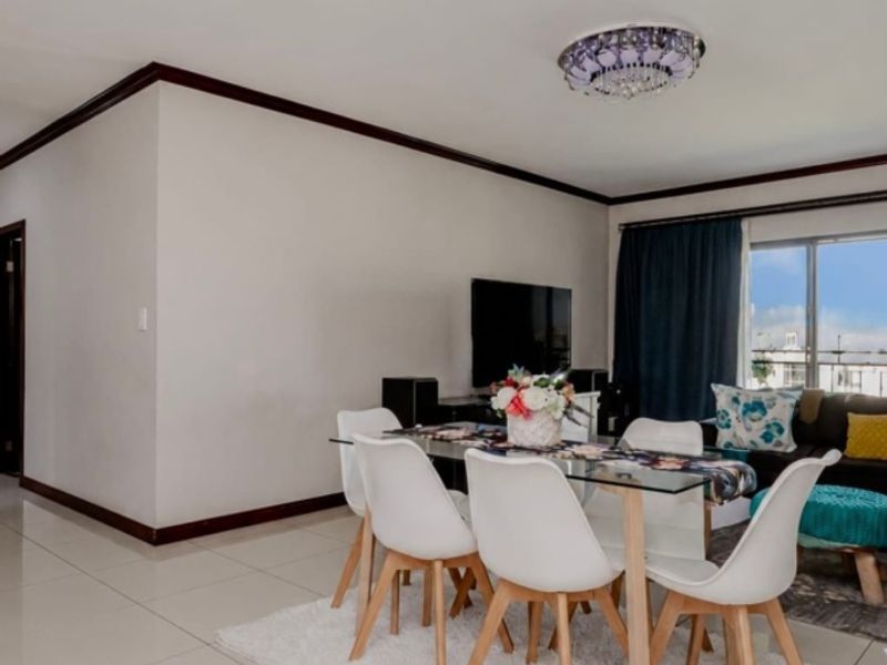 An open-plan living and dining area featuring neutral tiled flooring, crown molding, and a sliding glass door providing natural light.