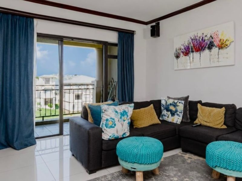 A bright living room featuring polished tile flooring, crown molding, and a sliding glass door providing access to a private balcony.