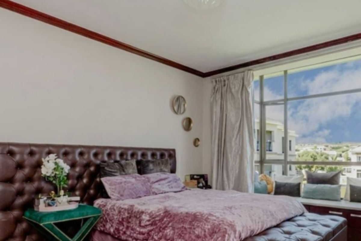 A well-maintained bedroom featuring laminate flooring, crown molding, and a large window with a built-in window seat offering natural light.