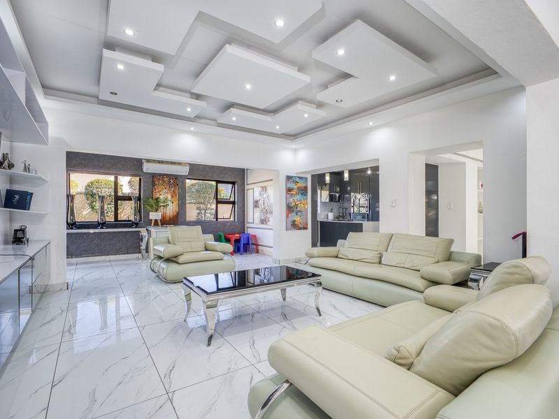 Spacious open-plan living area featuring a modern layered bulkhead ceiling, polished marble-look floor tiles, and integrated media cabinetry with recessed lighting.