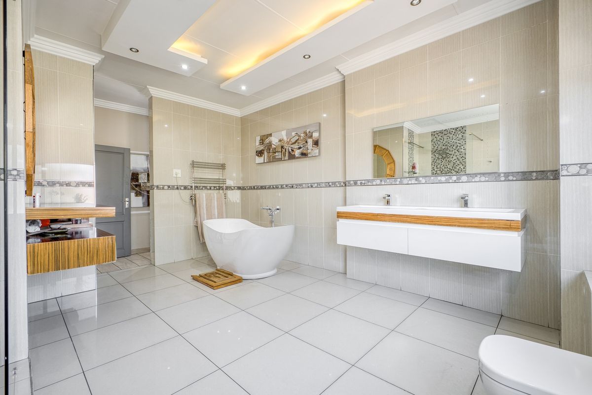 Modern, spacious bathroom featuring a sleek freestanding bathtub, double vanity with wall-mounted cabinetry, and elegant tiled finishes with recessed ceiling lighting.