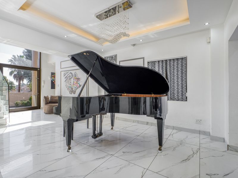 Spacious living area featuring high-gloss marble-look floor tiles, a recessed ceiling with modern lighting, and a glass staircase balustrade leading to the upper level.