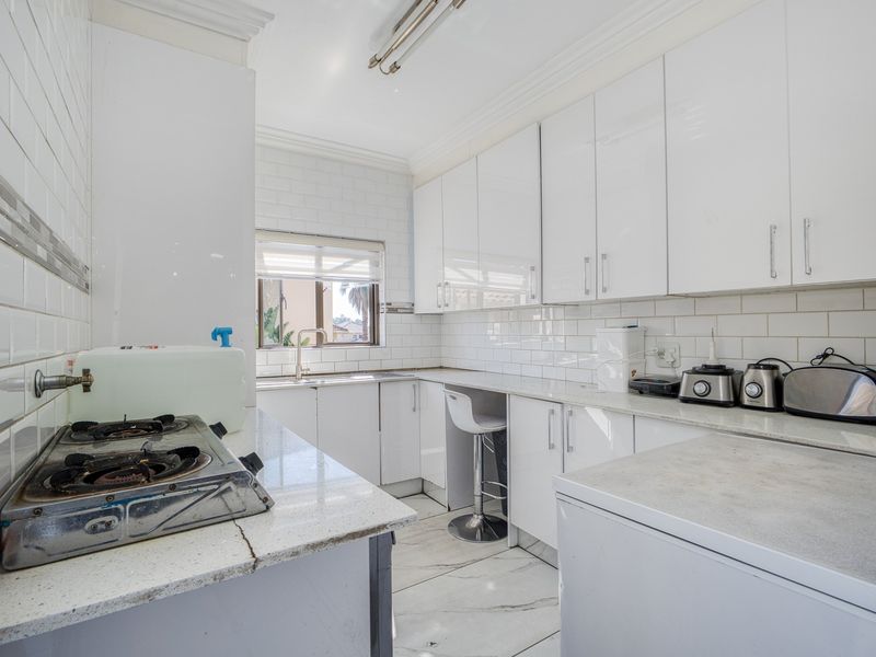 A functional kitchen featuring white gloss cabinetry, subway tile backsplash, stone countertops, and marble-look floor tiles with a dedicated sink area.