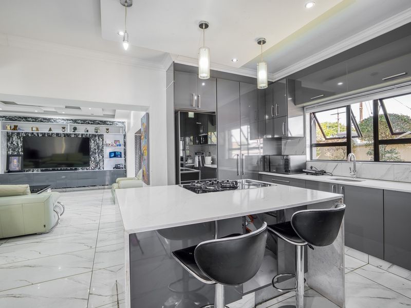 Modern open-plan kitchen and living area featuring high-gloss grey cabinetry, a central island with gas cooktop, and elegant marble-look tiled flooring throughout.