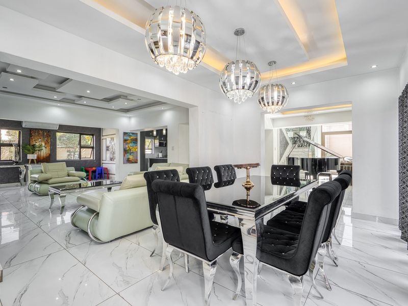 Spacious open-plan living and dining area featuring high-gloss marble-look flooring, modern coffered ceilings with recessed lighting, and elegant pendant chandeliers.