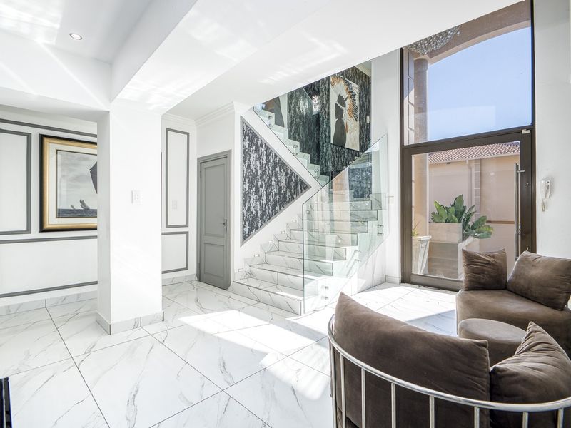 A bright and modern entrance hall featuring marble-look floor tiles, a striking glass balustrade staircase, and elegant wall molding with high ceilings.